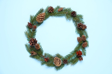 Christmas wreath made of fir branches and cones on light blue background, top view