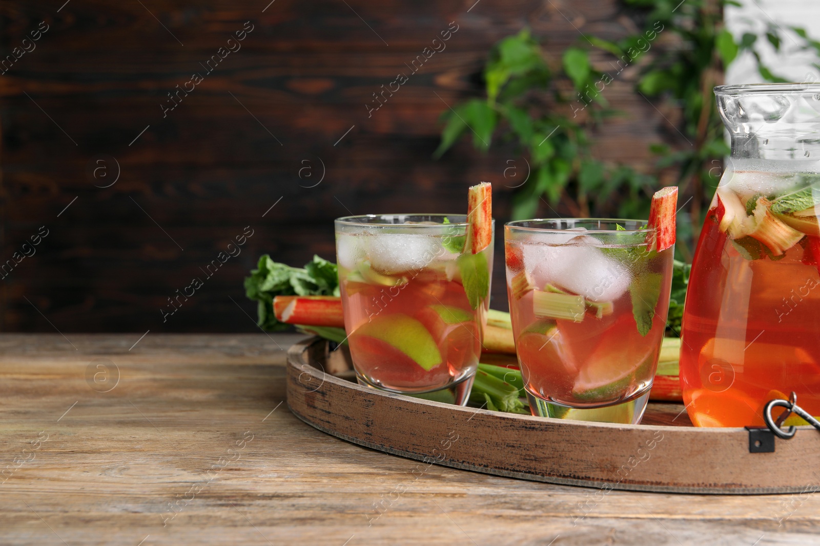 Photo of Glasses and jug of tasty rhubarb cocktail with citrus fruits on wooden table, space for text