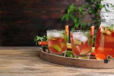 Glasses and jug of tasty rhubarb cocktail with citrus fruits on wooden table, space for text