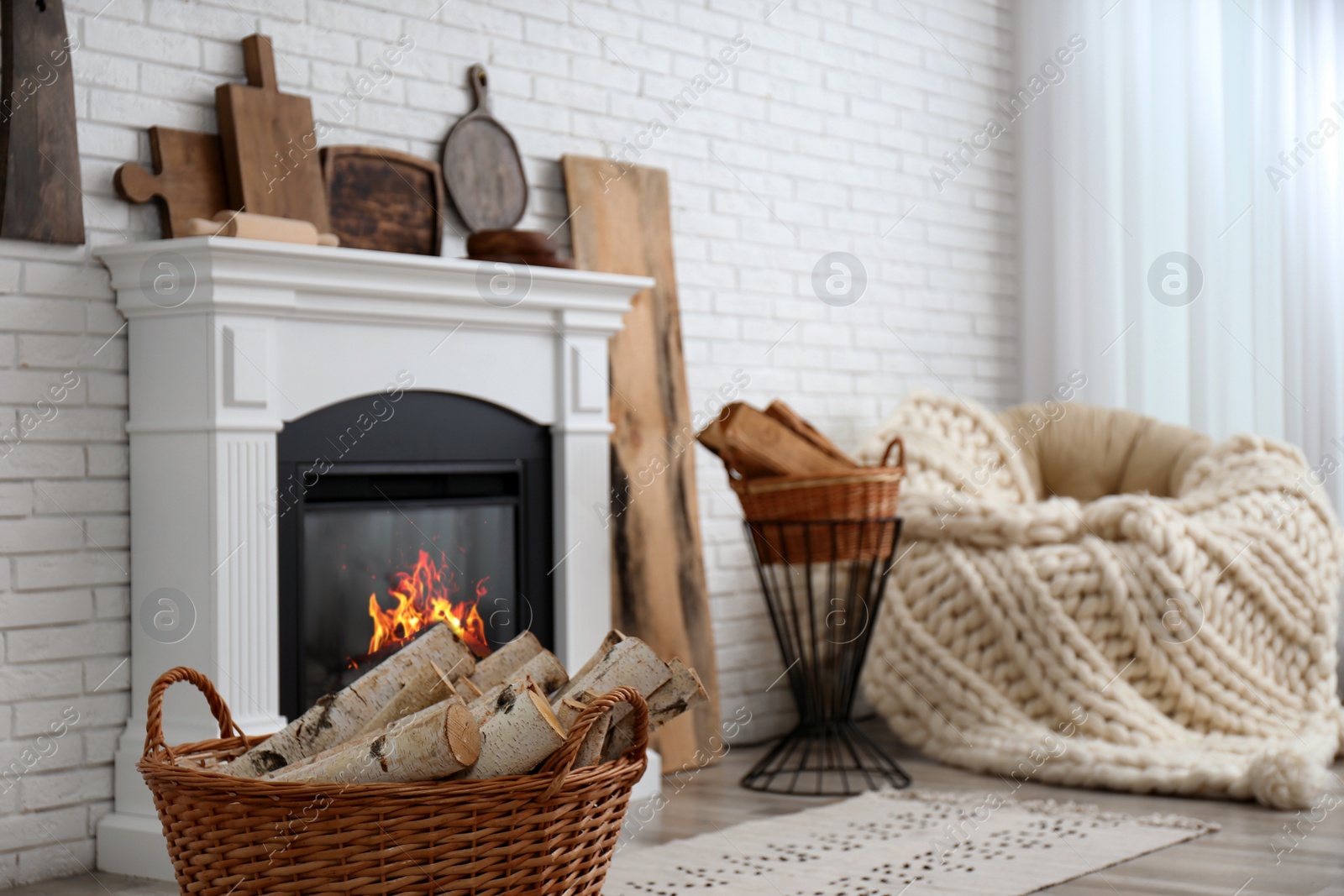 Photo of Wicker baskets with firewood and burning fireplace in cozy living room