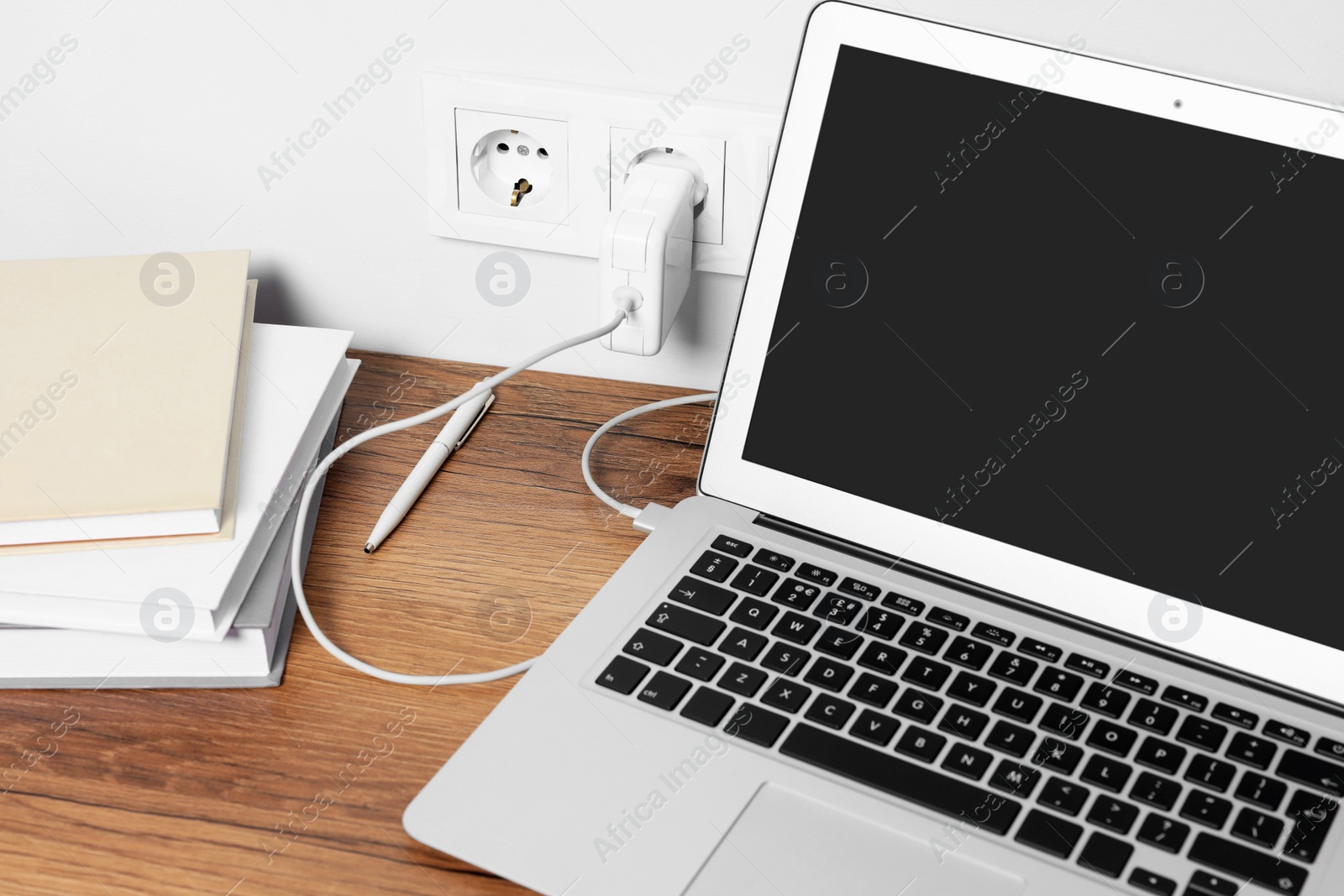 Photo of Modern new laptop charging on wooden table
