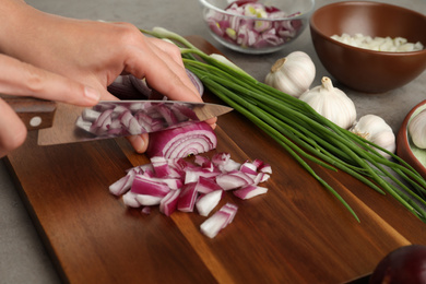 Woman cutting red onion on wooden board, closeup
