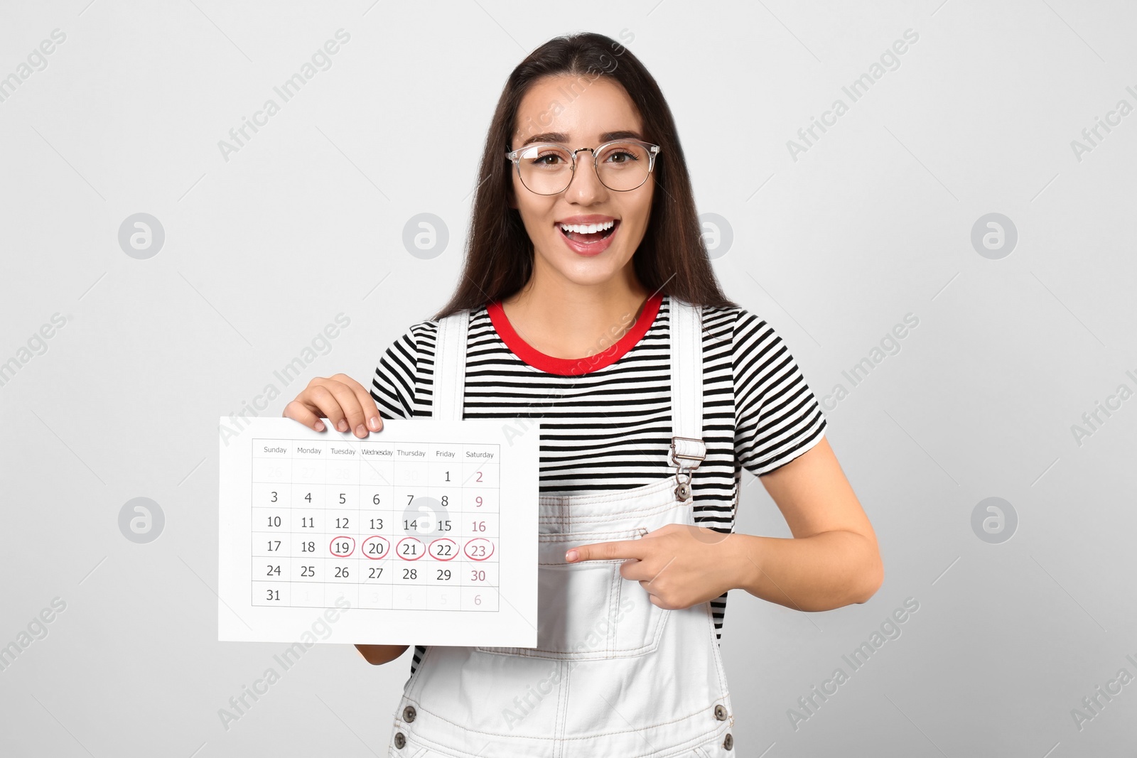 Photo of Young woman holding calendar with marked menstrual cycle days on light background