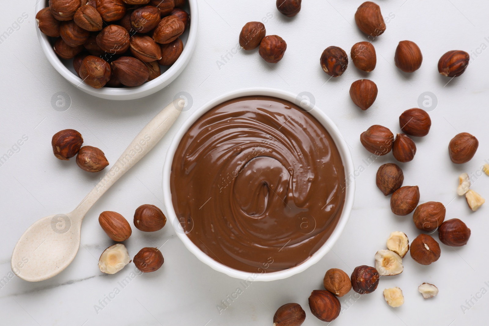 Photo of Bowl with chocolate paste and nuts on white marble table, flat lay