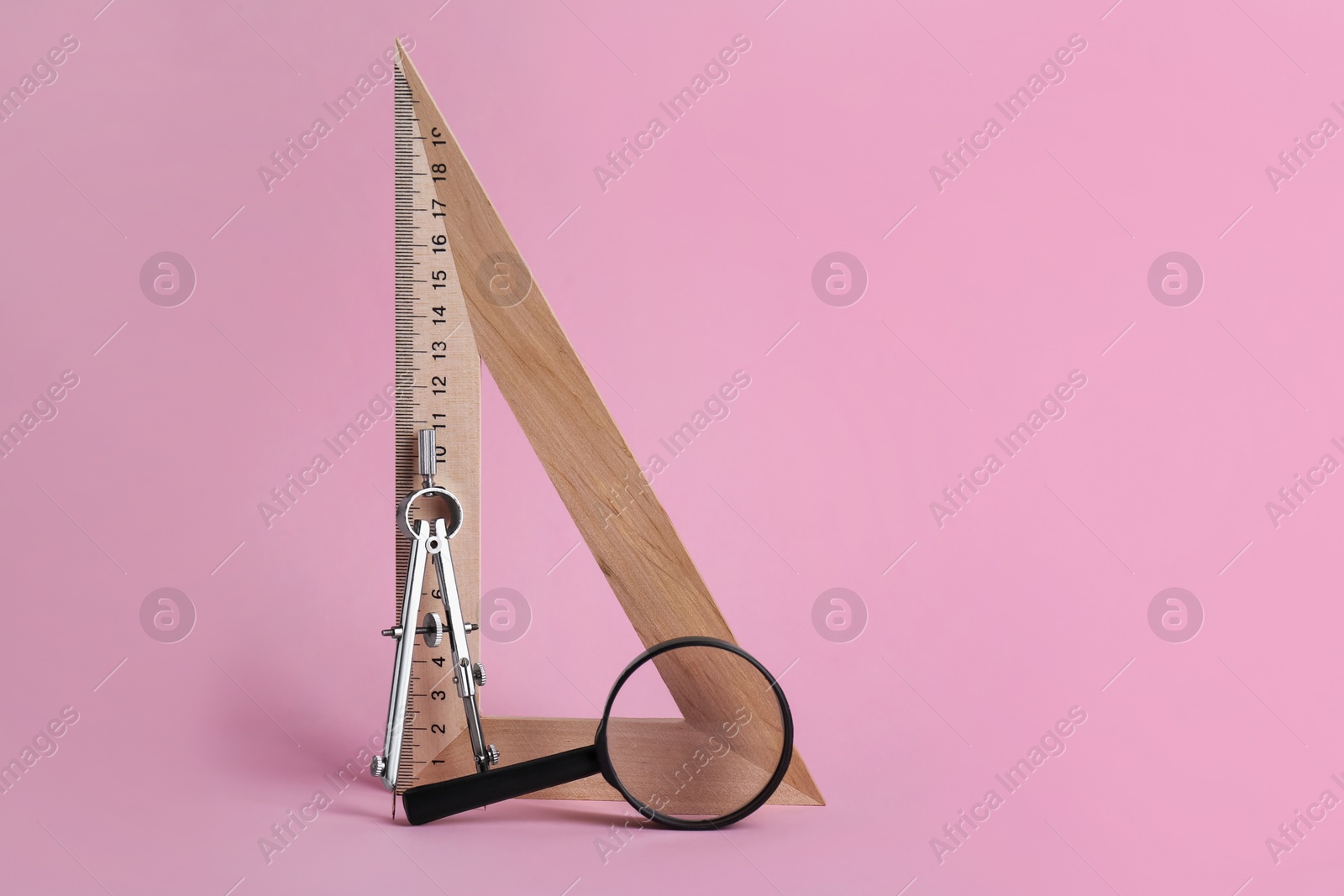 Photo of Triangle ruler, magnifying glass and compass on pink background