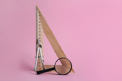 Photo of Triangle ruler, magnifying glass and compass on pink background