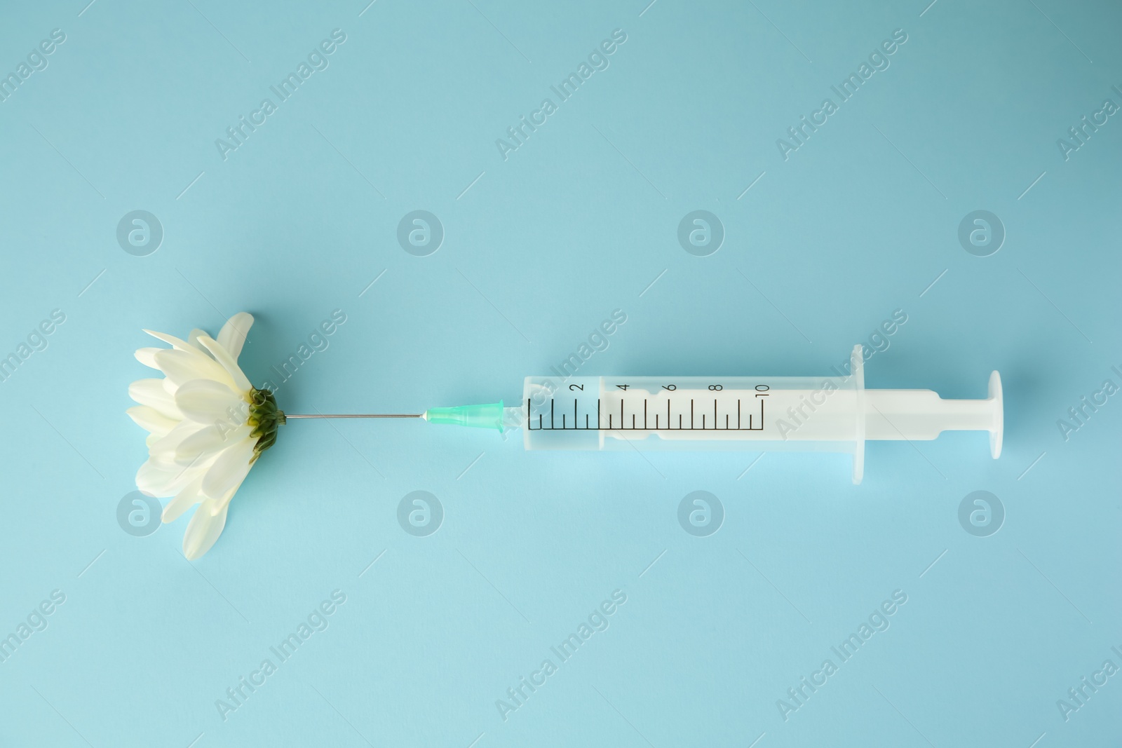 Photo of Medical syringe and beautiful chrysanthemum flower on light blue background, top view