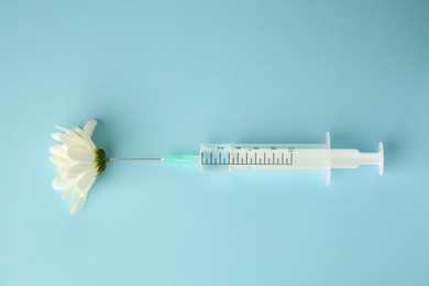 Medical syringe and beautiful chrysanthemum flower on light blue background, top view