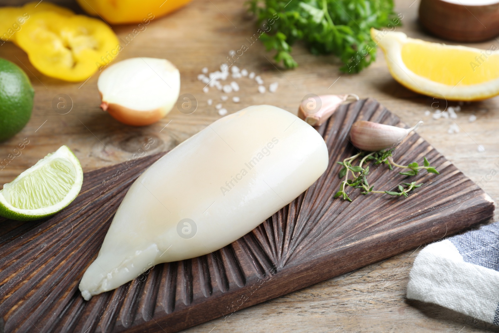 Photo of Fresh raw squid tube with lime, thyme and garlic on wooden table, closeup