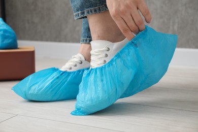 Woman wearing blue shoe covers onto her sneakers indoors, closeup