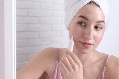 Photo of Woman with acne problem applying cream near mirror indoors