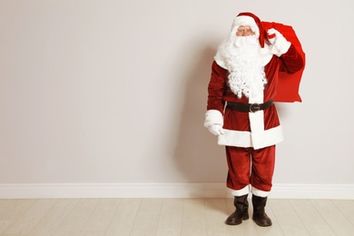 Photo of Authentic Santa Claus with bag full of gifts against grey wall. Space for text
