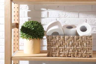 Photo of Toilet paper rolls in wicker basket and floral decor on wooden shelf against white brick wall