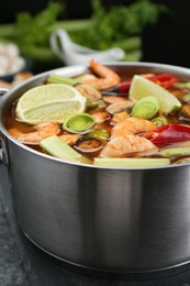Photo of Saucepan with delicious Tom Yum soup and ingredients on black marble table, closeup