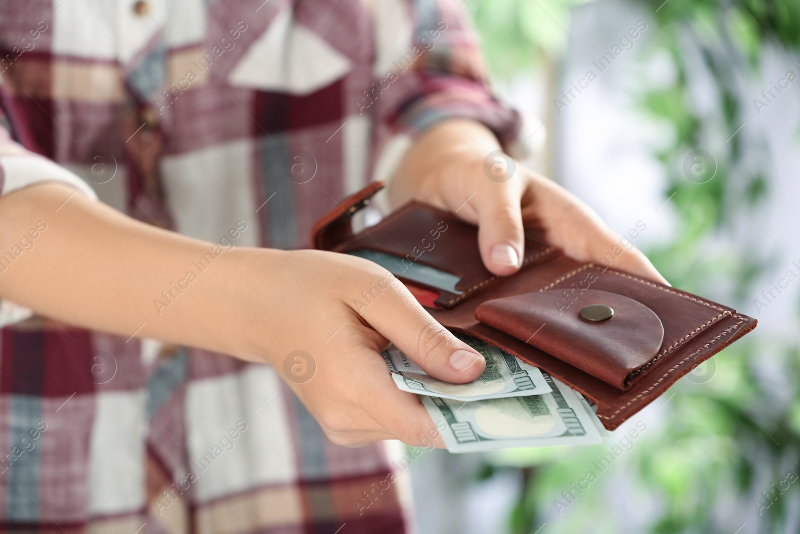 Photo of Woman putting money into wallet on blurred background, closeup