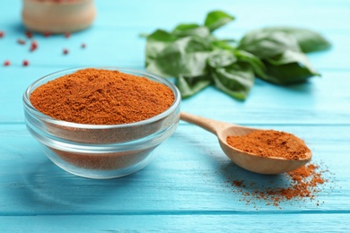 Photo of Glass bowl of red powdered pepper and spoon on blue wooden table, space for text