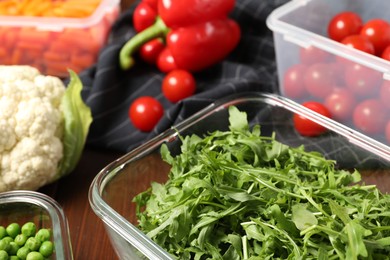 Photo of Containers with arugula and fresh products on table, closeup. Food storage