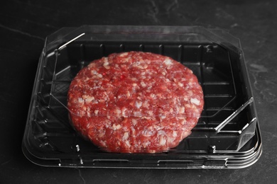 Photo of Plastic container with raw meat cutlet for burger on black table