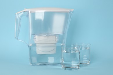 Filter jug and glasses with purified water on light blue background