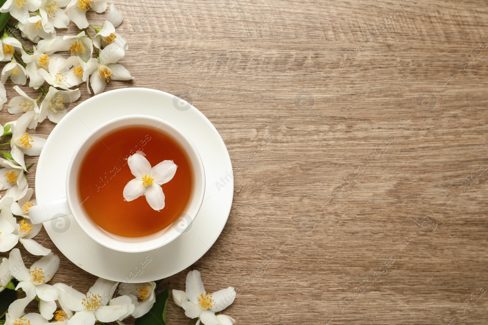 Photo of Cup of aromatic jasmine tea and fresh flowers on wooden table, flat lay. Space for text