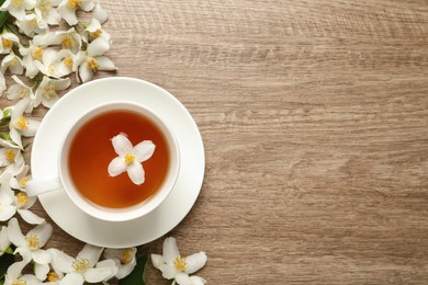 Cup of aromatic jasmine tea and fresh flowers on wooden table, flat lay. Space for text