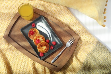 Tasty breakfast served in bedroom. Cottage cheese pancakes with fresh raspberries and sour cream on wooden tray, top view
