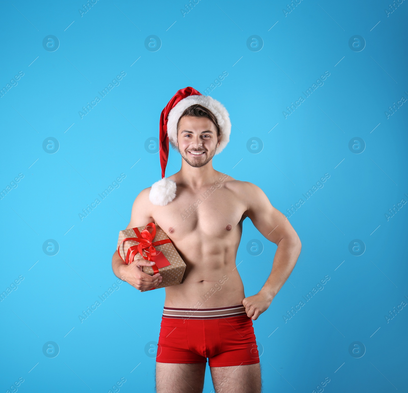 Photo of Shirtless sexy young Santa Claus with gift on color background