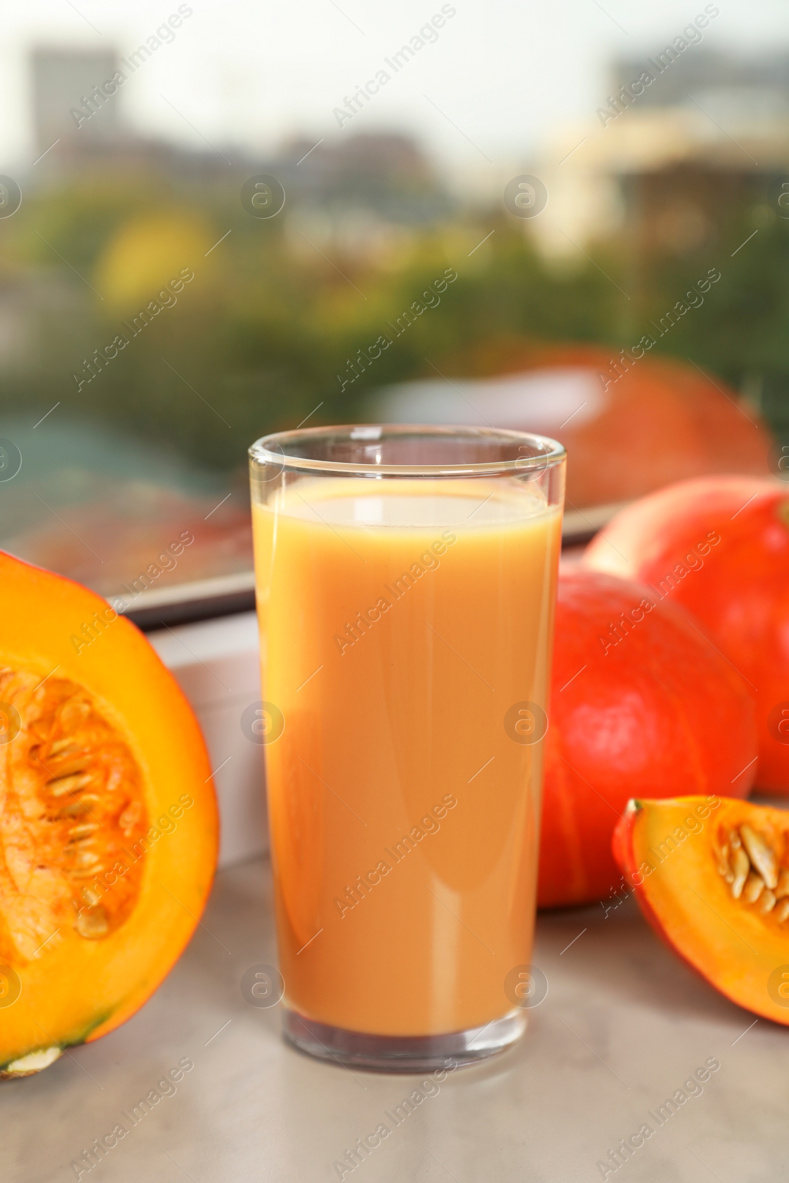 Photo of Tasty pumpkin juice in glass, whole and cut pumpkins on windowsill indoors