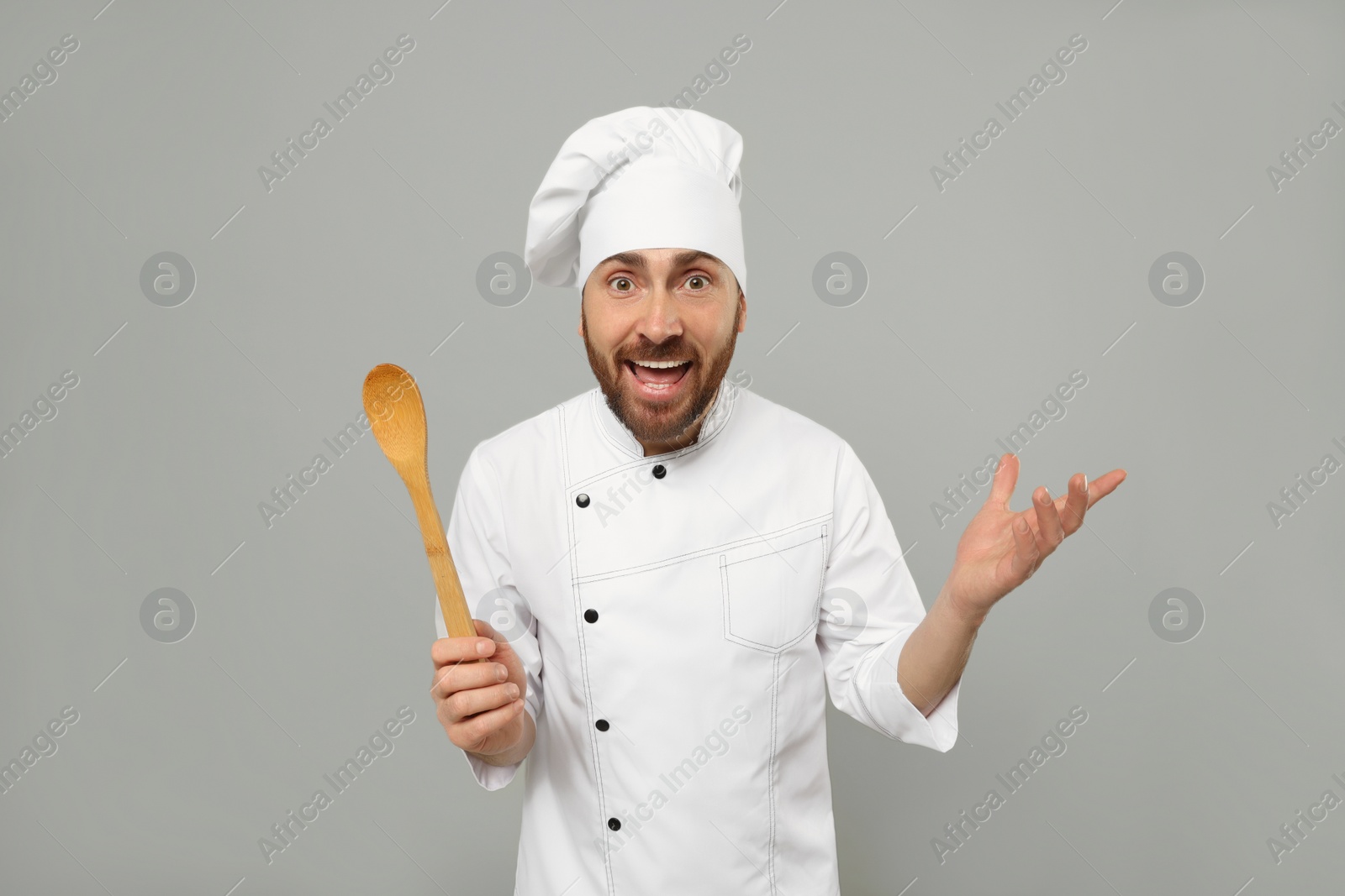 Photo of Emotional mature male chef with spoon on grey background