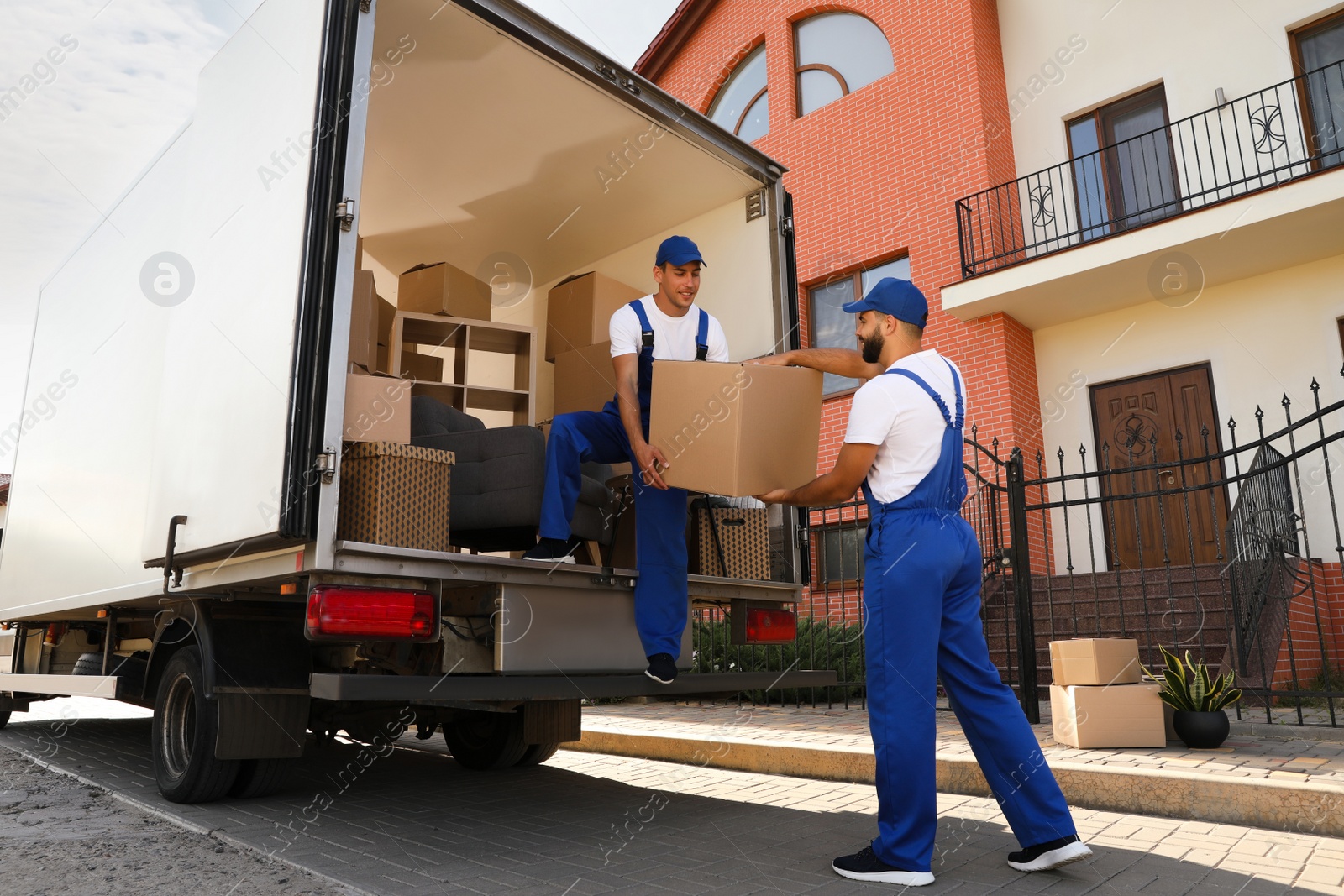 Photo of Workers unloading boxes from van outdoors. Moving service