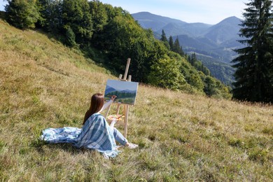 Photo of Young woman drawing on easel in mountains, back view. Space for text