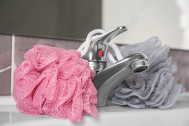 Photo of Colorful shower puffs between faucet on sink in bathroom, closeup