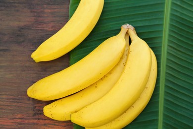 Photo of Delicious bananas and green leaf on wooden table, top view
