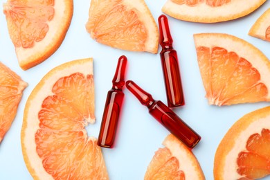 Skincare ampoules with vitamin C and slices of grapefruit on light blue background, flat lay