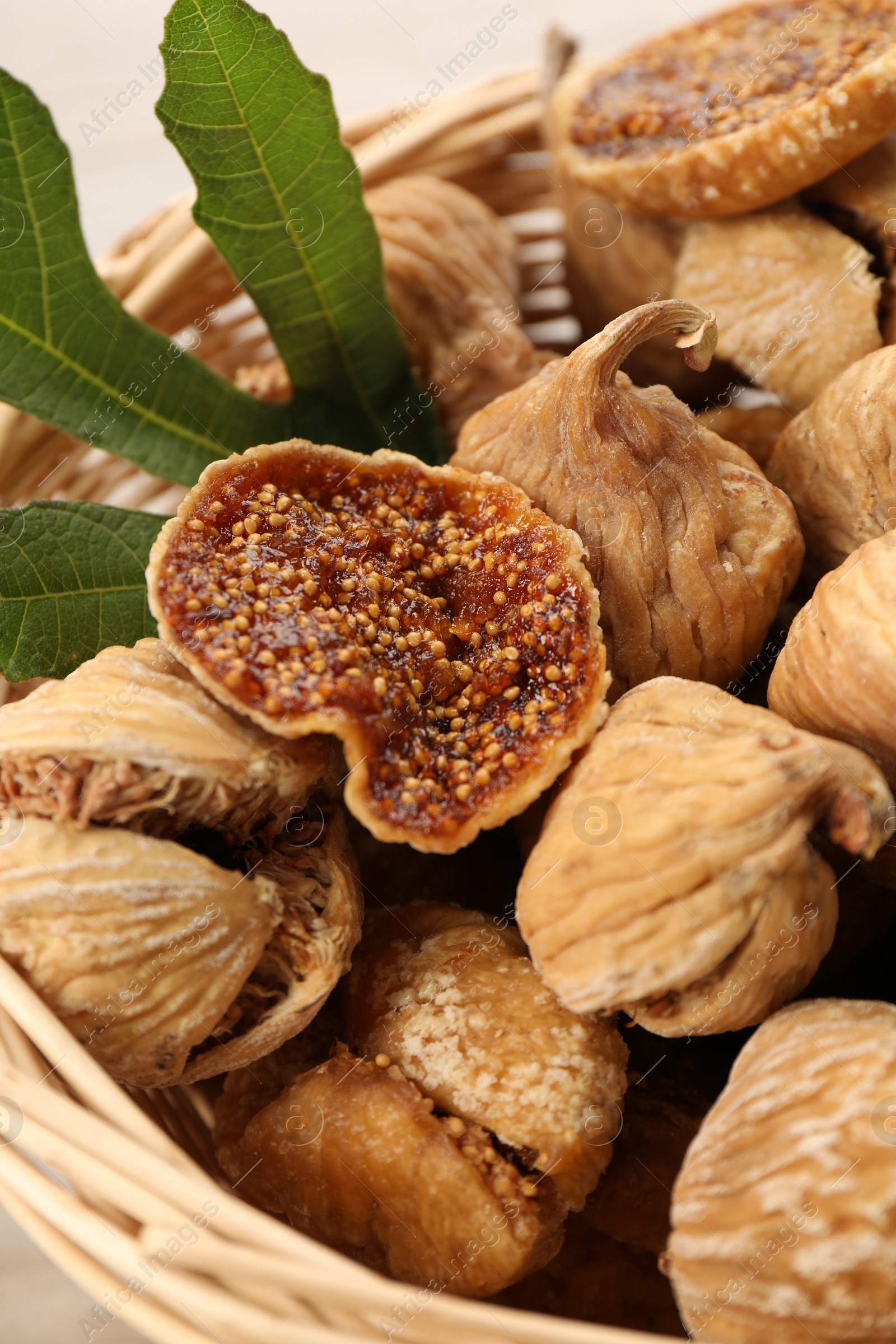 Photo of Wicker basket with tasty dried figs and green leaf on table, closeup