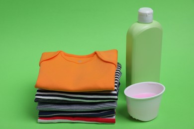 Photo of Stack of baby clothes and laundry detergents on light green background