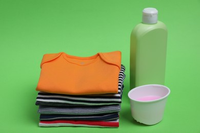 Stack of baby clothes and laundry detergents on light green background