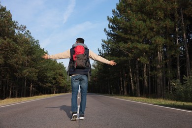 Man with backpack going along road near forest, back view