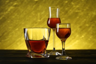 Different delicious liqueurs in glasses on dark wooden table