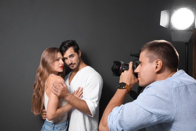 Professional photographer taking picture of young couple on dark grey background in modern studio