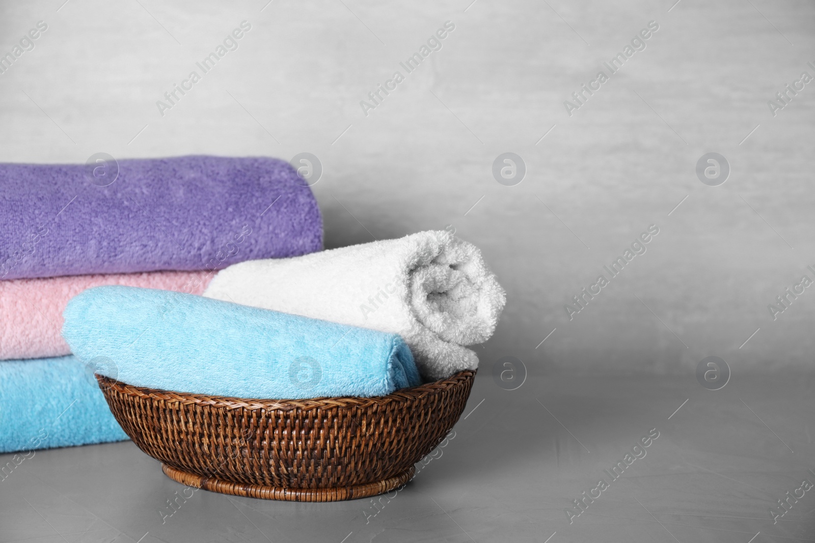 Photo of Wicker basket with rolled bath towels on grey table. Space for text