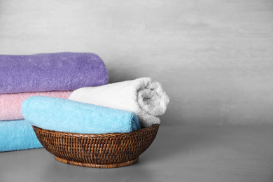 Photo of Wicker basket with rolled bath towels on grey table. Space for text