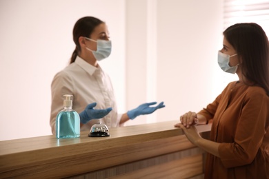Photo of Receptionist with client at countertop in hotel, focus on dispenser bottle of antiseptic gel and service bell