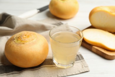 Photo of Glass of fresh natural turnip juice, cut and whole roots on white table