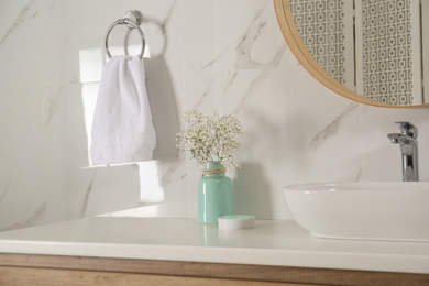 Vase with flowers and soft towel in bathroom interior