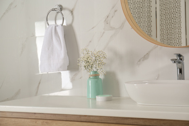 Photo of Vase with flowers and soft towel in bathroom interior