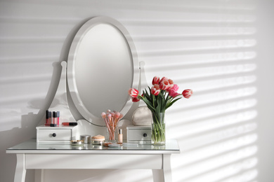Photo of Elegant dressing table with makeup products, accessories and tulips indoors. Interior element