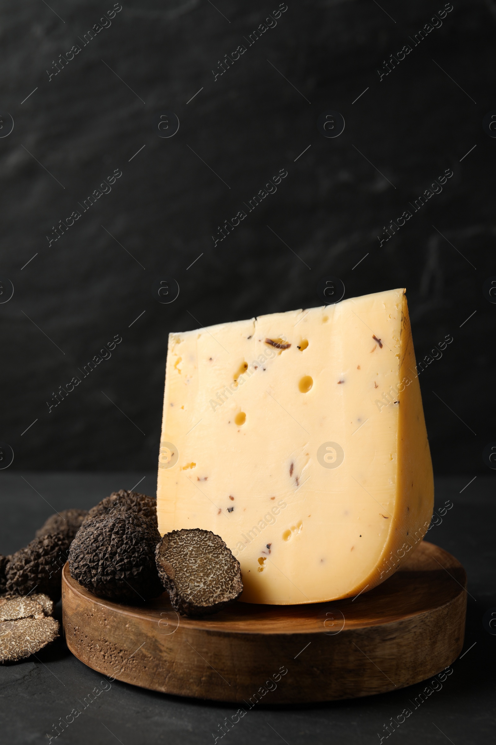 Photo of Wooden board with delicious cheese and fresh truffles on black table. Space for text