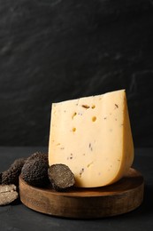 Photo of Wooden board with delicious cheese and fresh truffles on black table. Space for text