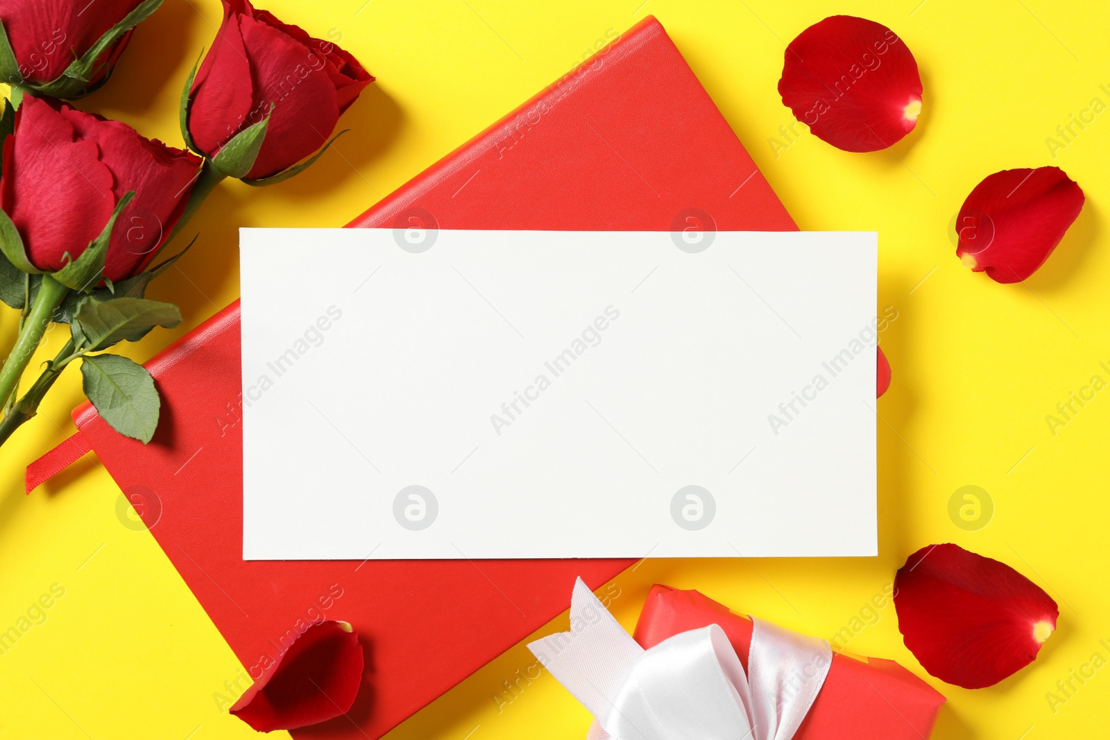 Photo of Flat lay composition with blank greeting card, notebook and roses on yellow background. Valentine's day celebration